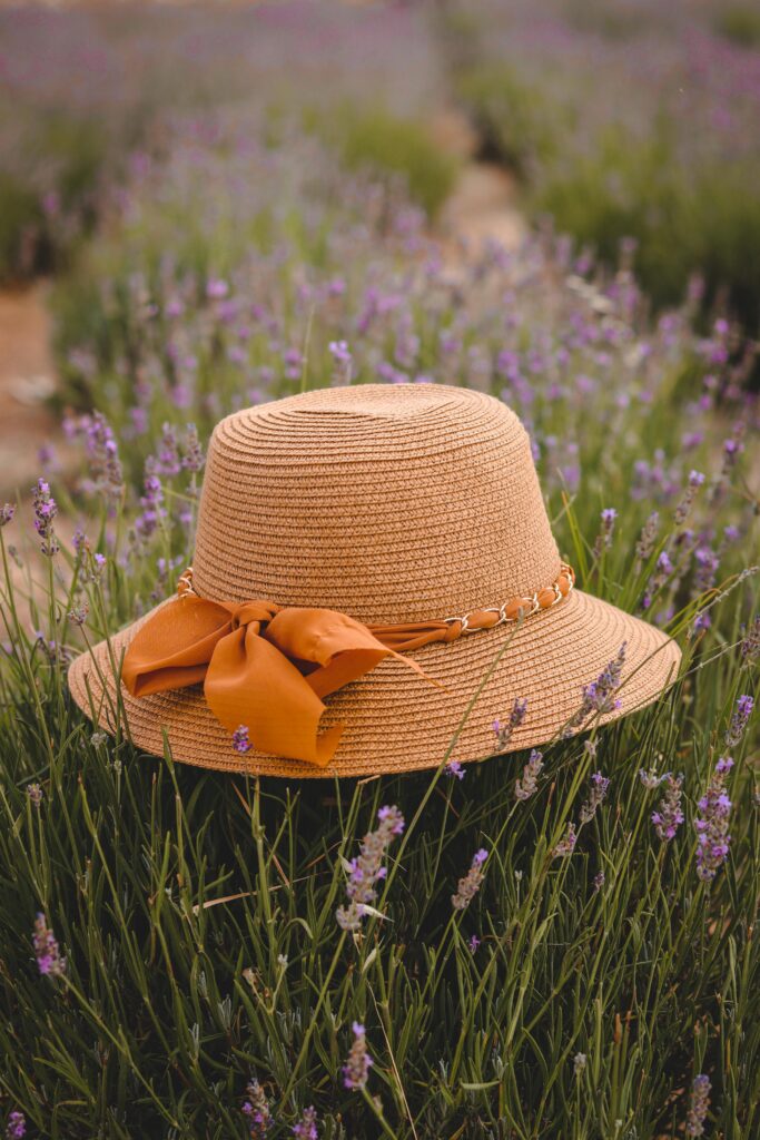 A straw hat with a ribbon placed in a serene lavender field during daytime.