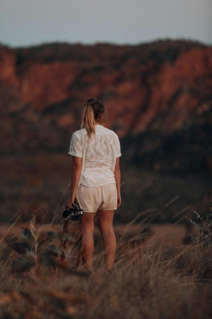 Back view of a woman standing in nature holding a camera, showcasing adventure and exploration.