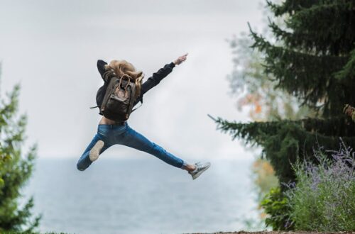 Energetic woman leaping in outdoor forest setting with lake view, showcasing freedom and joy.