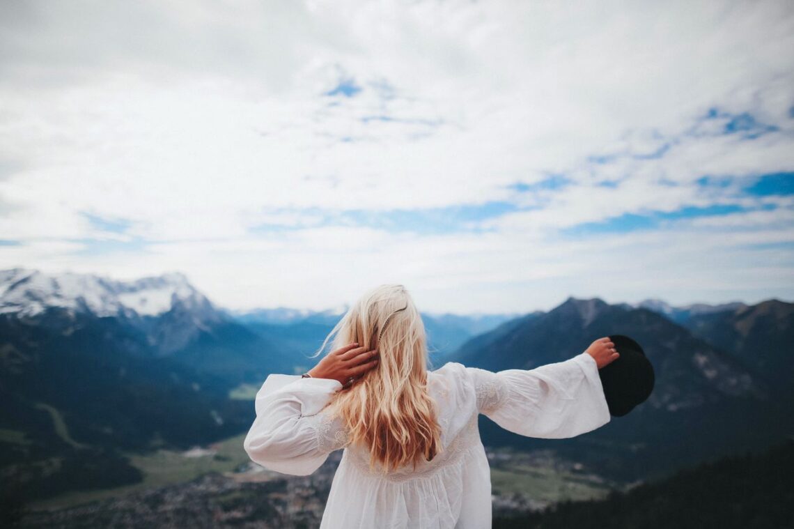 Blonde woman in a white dress overlooks the beautiful mountain landscape of Ohlstadt, Germany.