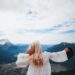 Blonde woman in a white dress overlooks the beautiful mountain landscape of Ohlstadt, Germany.