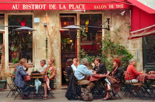 The Art of Small Talk, French Edition Outdoor seating at a bustling Parisian bistro, capturing lively conversation and vibrant atmosphere.
